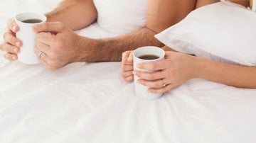 casal com xícaras de chá na cama.