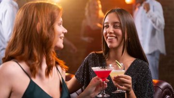 amigas em bar, brindando com bebidas em mãos.
