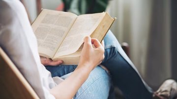 Pessoa sentada com livro no colo e lendo