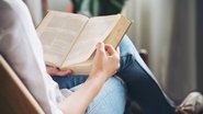 Pessoa sentada com livro no colo e lendo