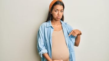 mulher grávida com mãos sob a barriga e expressão triste.