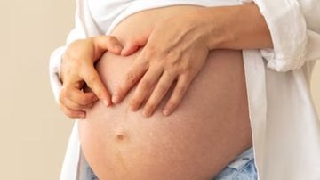 mulher grávida com as mãos sob barriga.