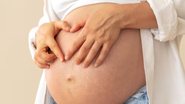 mulher grávida com as mãos sob barriga.