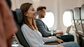 mulher sentada em poltrona de avião e sorrindo.