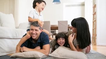 pais e filhos rindo na sala de casa, deitados no chão.