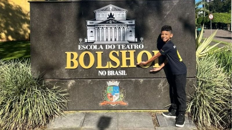 bailarino mirim em frente a placa da escola de dança