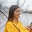 Mulher rindo na chuva com celular na mão