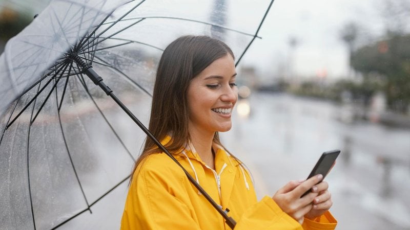 Mulher rindo na chuva com celular na mão