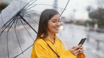 Mulher rindo na chuva com celular na mão