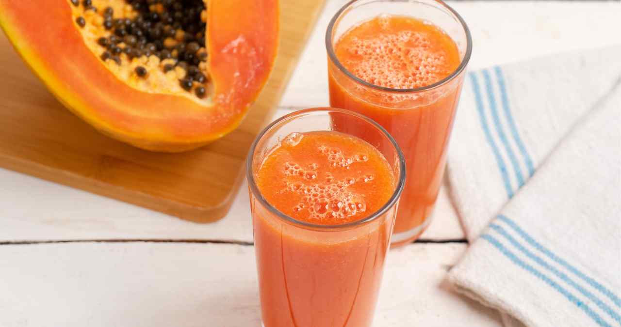 dois copos de suco de mamão ao lado de uma banda cortada da fruta