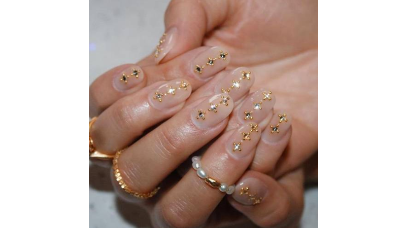 Unhas nude com aplicações douradas.