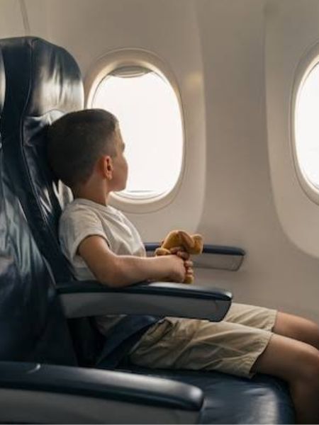 criança sentada em poltrona de avião, olhando pela janela.
