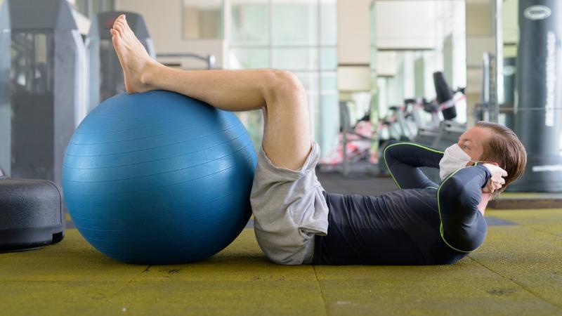 homem na academia realizando exercicios fisicos com mascara de protecao