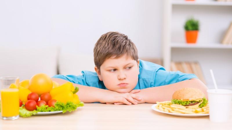 criança acima o peso olhando para comida de fast-food