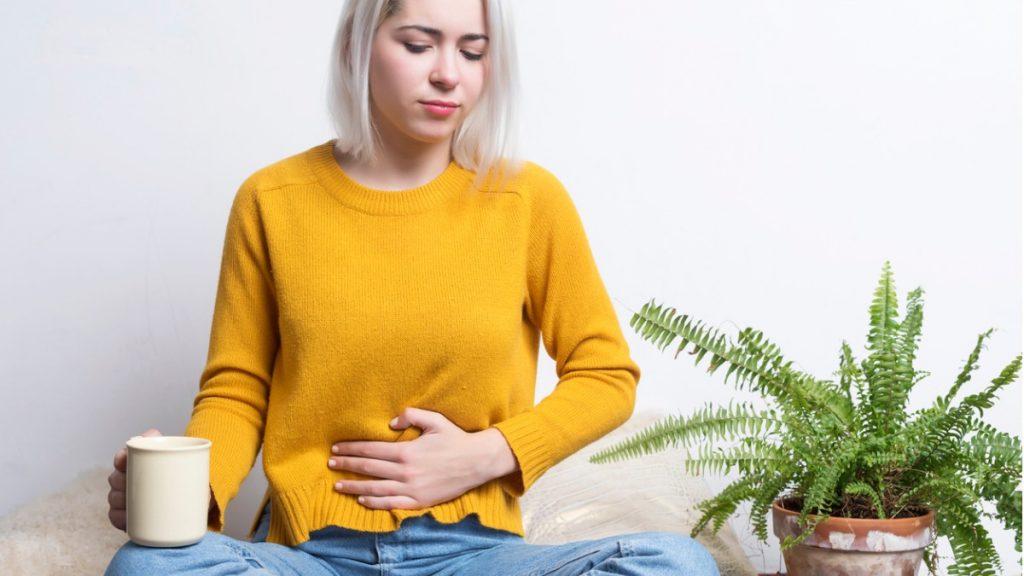 mulher com cólica tomando chá para descer a menstruação 